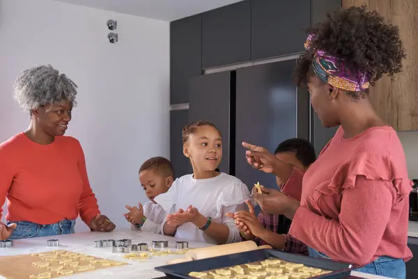 African family talking while cutting cookie shapes in a cookie dough in the kitchen. Horizontal extended family.