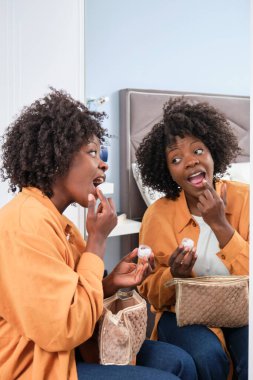 Mutlu Afrikalı kadın aynanın karşısına dudak kremi sürüyor..