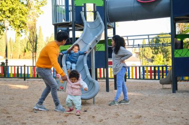 İspanyol aileler çocuklarıyla parkta kaydırak oynuyorlar. Latin ailesi.