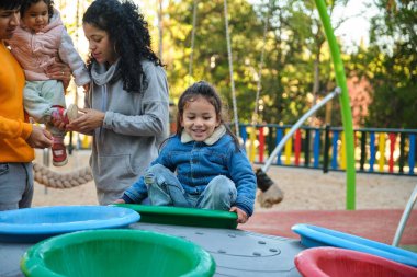 Latin çocuk oyun parkında oynuyor, ailesi arka planda. İspanyol ailesi..