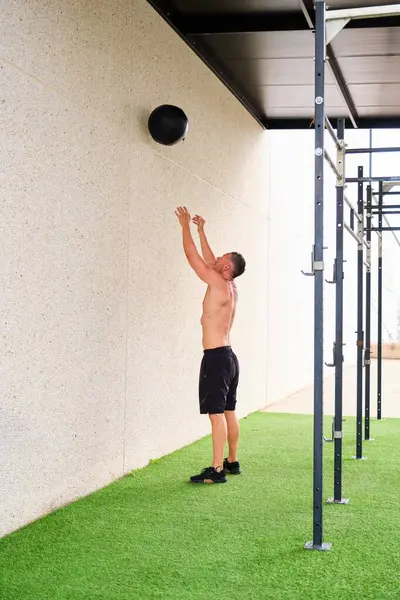 Man throwing medicine ball against wall and squat in cross training outdoor gym. Cross fit, fitness and sport.