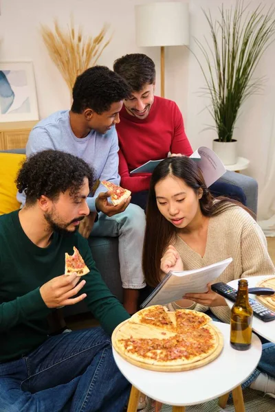 Group of multiethnic university colleagues studying and eating pizza together at shared students house.