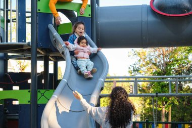 İspanyol aileler çocuklarıyla parkta kaydırak oynuyorlar. Latin ailesi.
