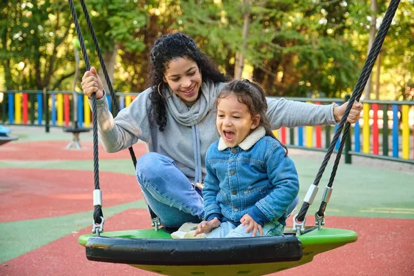 Happy Latin mother playing with her son on a swing in a park. Latin family.