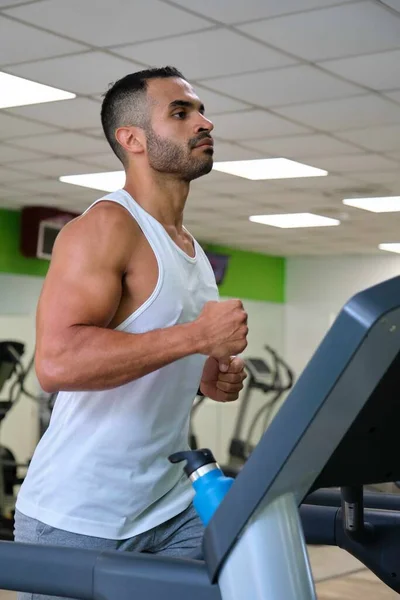 Strong Hispanic man running on treadmill at a gym.