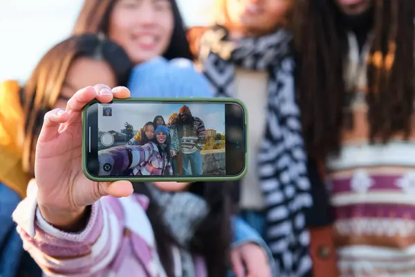 Smartphone screen view of multiracial group of friends taking a selfie at street in autumn.