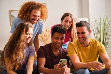 Bir grup neşeli çoklu etnik arkadaş akıllı telefon ekranında komik içerikler izliyorlar..