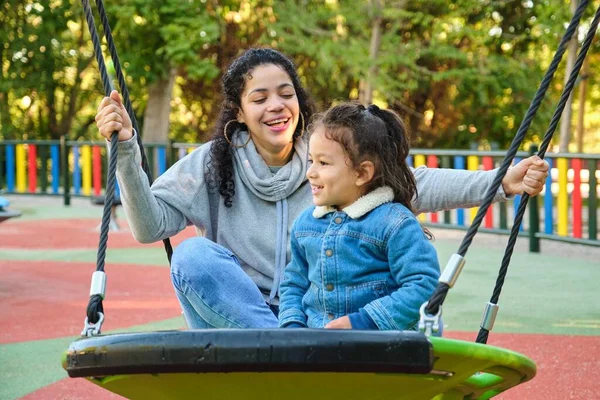 Happy Latin mother playing with her son on a swing in a park. Latin family.
