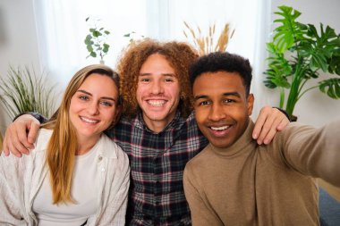 Üç farklı etnik gruptan mutlu arkadaş evde selfie çekiyorlar. Gülümseyen insanlar portresi.