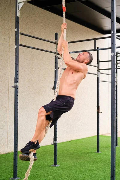 Man performing rope climbs in a outdoor fitness gym. CrossFit, fitness and sport.