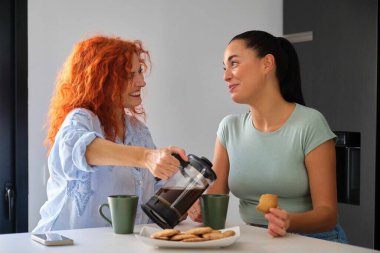 Anne ve kızı birlikte kahvaltı yapıyor, tereyağlı kurabiye ve kahve yiyorlar. Aile zamanı..