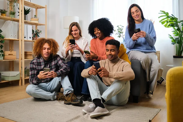 Group of young flat mates using their smartphone together at shared apartment.