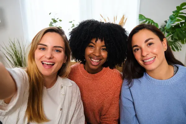 Üç farklı etnik gruptan mutlu bayan arkadaş evde selfie çekiyorlar. Gülümseyen insanlar portresi.