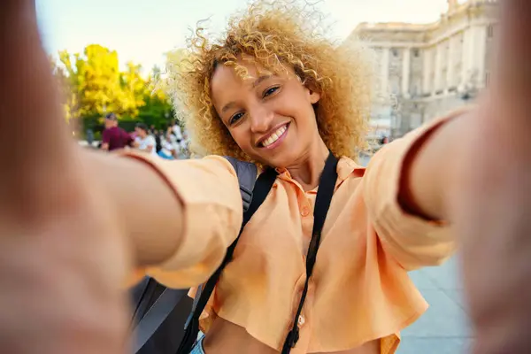 Brazilian female tourist smiling and doing a selfie while sightseeing in Madrid, Spain.