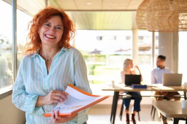 Orta yaşlı mutlu iş kadını iş yerinde kameraya bakıyor..