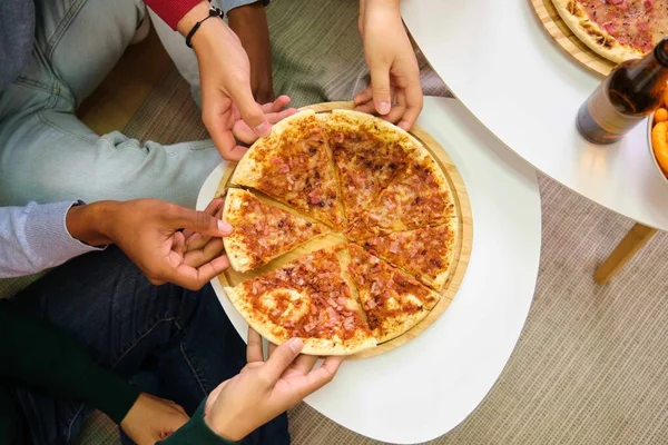 Top view of friends hands grabbing a BBQ pizza slice in a shared flat.