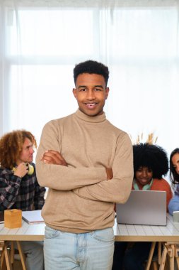 Genç Afrikalı adam kameraya bakıp gülümsüyor ve üniversite arkadaşlarıyla arka planda ders çalışıyor..