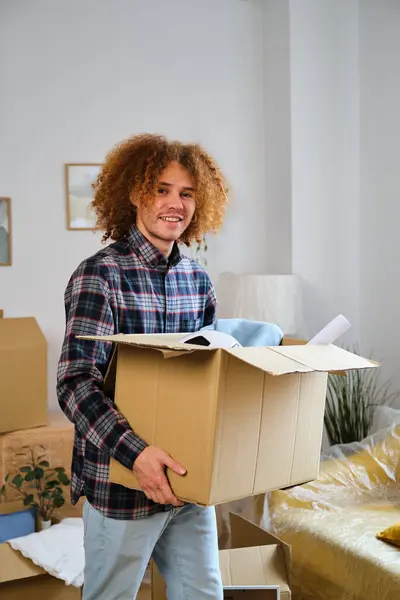 Latin man holding a moving cardboard box to settle in his new home. Student residence relocation.