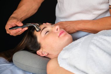 Yüz masajı yaptıran kadın, yüz soğutma metal silindirli. Profesyonel cilt bakımı.