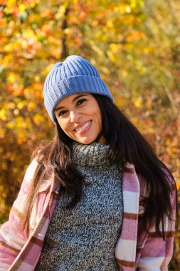 Güneşli bir sonbahar gününde parkta gülümseyen ve kameraya bakan genç bir Latin kadının portresi..