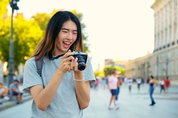Taiwanese male tourist smiling and looking at photos in his camera while sightseeing in Madrid, Spain.