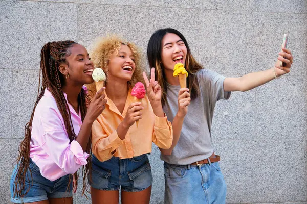 Three multiracial happy friends with ice creams taking a selfie in summer at street.