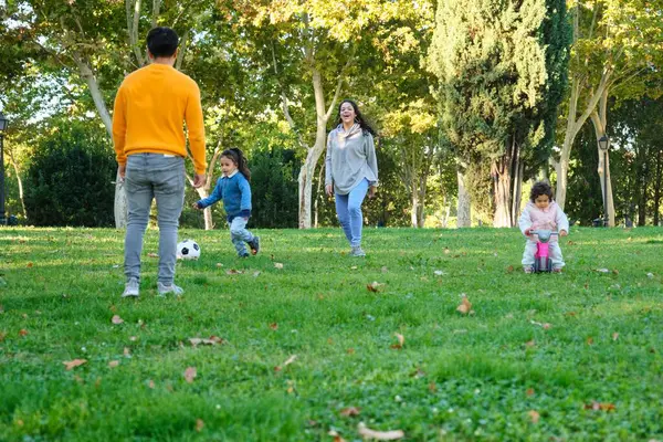 Latin family with two children playing soccer and with balance bike in a park. Hispanic family.
