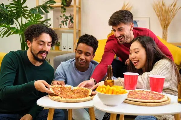 Group of happy multiracial friends eating pizza in a shared student house.