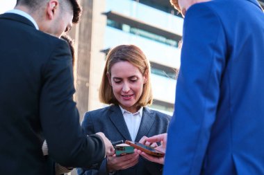 Bir grup meşgul uluslararası iş adamı akıllı telefonlarını sokakta kullanıyor..