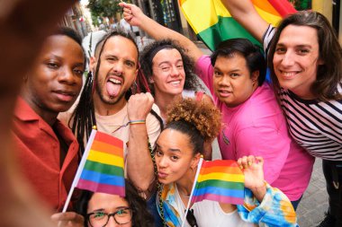 Gökkuşağı bayrakları taşıyan ve selfie için gülümseyen bir grup LGBTQ çalışanı. Sahne neşeli ve kutlayıcı, çünkü grup büyük ihtimalle bir gurur etkinliğine katılıyor..