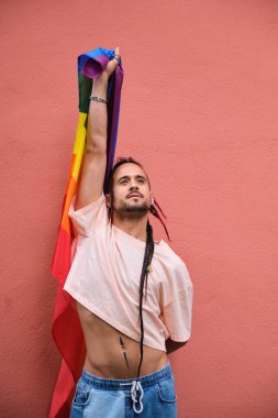 Rasta saçlı eşcinsel adam elinde gökkuşağı bayrağı tutuyor ve gururla gülümsüyor. Gurur ve mutluluk kavramı.