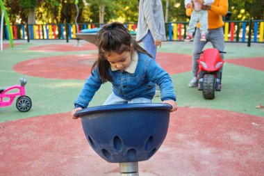 Üç yaşındaki Latin bir çocuk oyun parkında döner top oynuyor.