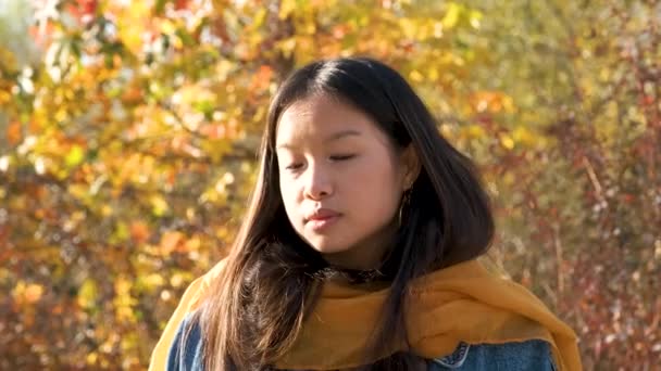 若いアジアの女性が笑顔で秋の公園でカメラを見る — ストック動画