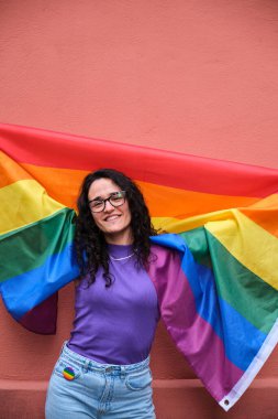 Lezbiyen kadın elinde gökkuşağı bayrağı ve gülümseyerek Onur Ayı 'nı kutluyor..