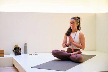 Bir kadın mindere oturmuş yoga duası yapıyor. Rahatlamış ve odaklanmış durumda..