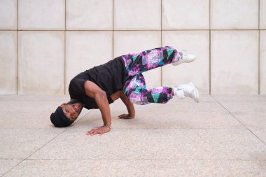 Bereli ve sokak kıyafetli genç adam dışarıda break dans yapıyor.