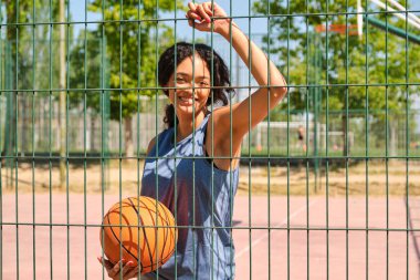 Genç bayan basketbolcu güneşli bir günde çitin yanında topla poz veriyor.