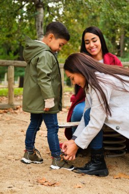 Latin bir anne, oğlunun çocuk parkında ayakkabı bağcıklarını bağlıyor. LGBT Ailesi.