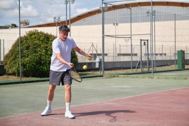 Son sınıf öğrencisi tenis oynarken tamamen konsantre oluyor. Güneşli bir günde raketiyle topa vuruyor.