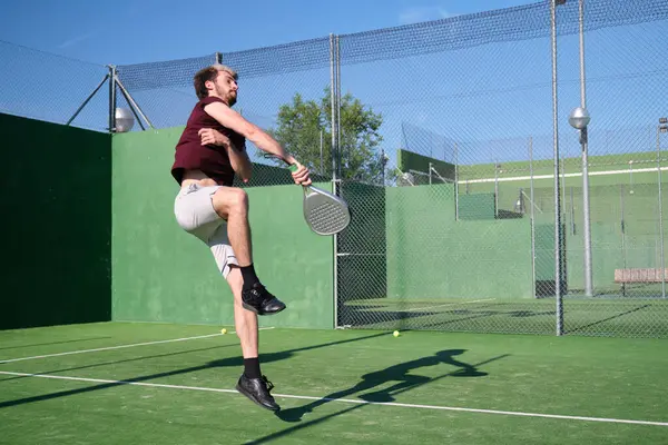 Genç adam güneşli bir yaz gününde kortta raket oynarken atlıyor.