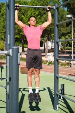 Odaklanmış sporcu güneşli bir günde barfiks çekerek vücudunun üst kısmını güçlendiriyor.