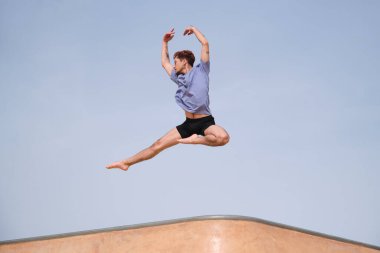 Kızıl saçlı genç adam mavi gökyüzünün önünde zarif bir şekilde zıplıyor.