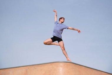 Dövmeli genç adam güneşli bir günde binanın tepesinde dans ederken zarifçe zıplıyor.