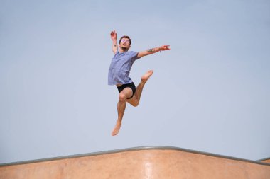 Genç adam bir kaykay parkında havaya zıplayarak koreografi yapıyor.