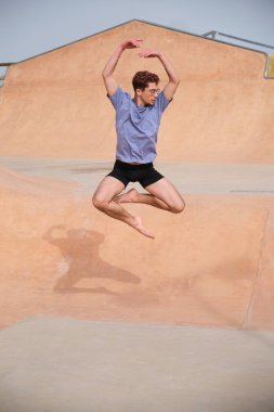 Kıvırcık saçlı genç adam zarif bir şekilde havaya zıplıyor. Yeteneğini ve dans tutkusunu şehir ortamında sergiliyor.