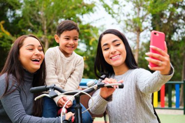 Oğluyla parkta selfie çeken mutlu Latin lezbiyen çift. LGBT Ailesi.
