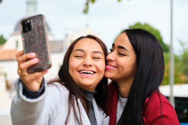 Mutlu Latin lezbiyen çift sokakta sarılıyor, gülüyor ve selfie çekiyor. LGBT çifti.