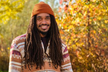 Afrika kökenli Amerikalı genç bir adam gülen ve güneşli bir sonbahar gününde kameraya bakıyor..