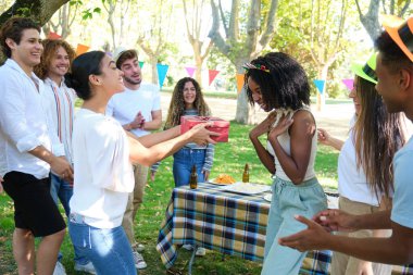 Bir grup arkadaş parkta doğum gününü kutluyorlar. Arkadaşları izlerken bir kadın hediye alıyor.