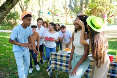 Bir grup neşeli genç, doğum günü bandı takan siyah bir kadın için parkta sürpriz bir doğum günü partisi veriyor.